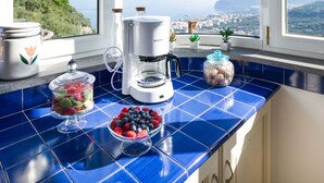 Eine Küche mit Kaffeemaschine, einer Nudelnapf und einer Schüssel Beeren auf einer blauen Fliesenarbeitsplatte.