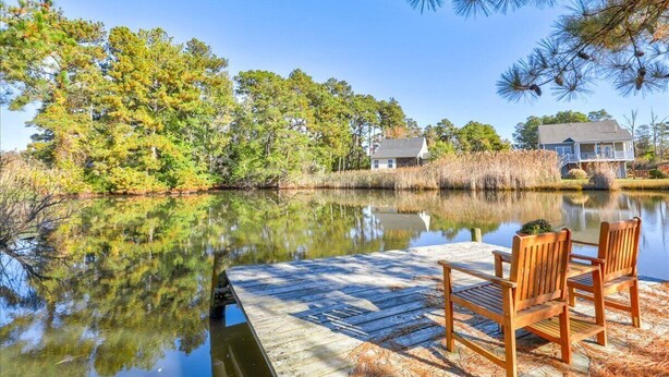 Une jetée en bois avec deux chaises, un lac paisible et une maison en arrière-plan.