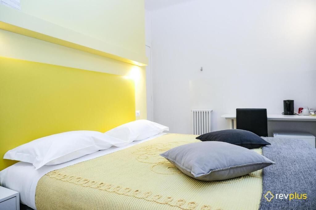 A hotel room with a bed, pillows, a desk, and a chair.