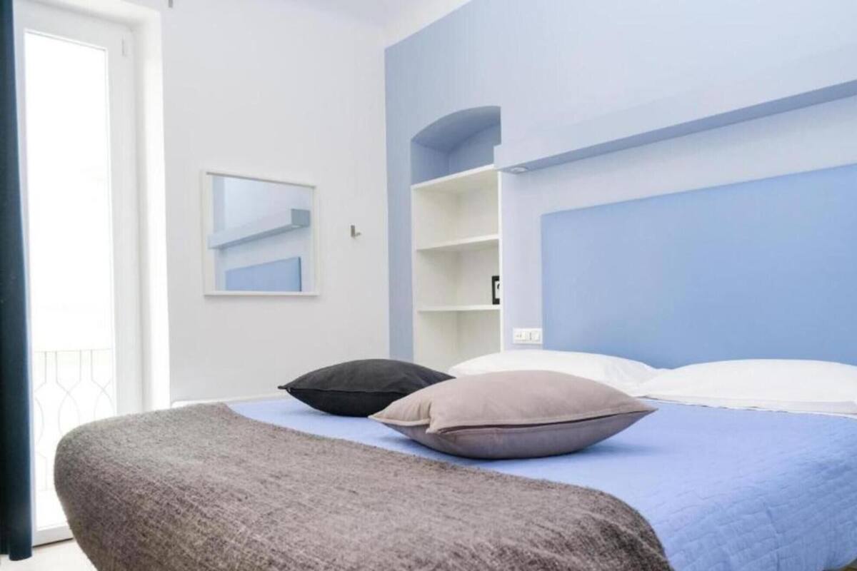 A bedroom with a bed, pillows, a bedside table, and a window.