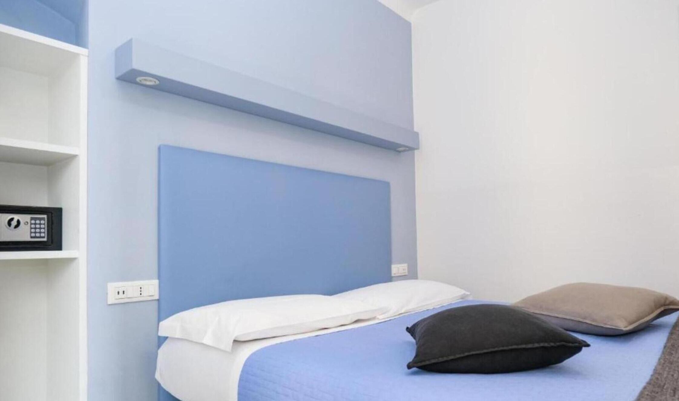 A room with a blue headboard, a white shelf with a black object, and a bed with white and black pillows.