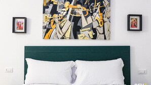A bedroom with a green headboard, white bedding, and a large abstract painting on the wall. - Lia Rooms Cinque Terre Wave (La Spezia)