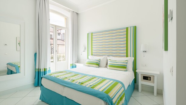 Un dormitorio con una cama grande, una mesita de noche, cortinas en una ventana y una lámpara de pared.
