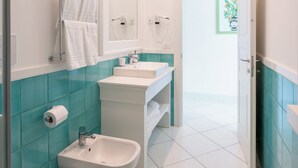 Un baño moderno con inodoro, bidé y lavamanos, con azulejos verde agua y blancos.