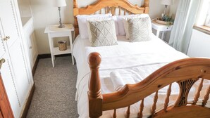 Une chambre d’hôtel bien rangée, avec un lit en bois, une table de chevet avec une lampe, une petite table de chevet avec un panier, et un tableau encadré au mur.