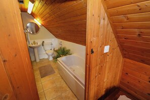 Ett badrum med träpanel på väggarna, utrustat med badkar, toalett, handfat och spegel.