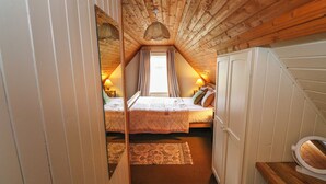 Une chambre mansardée chaleureuse avec deux lits, un plafond en bois et une petite salle de bain.