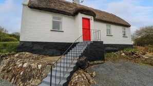 Une maison blanche avec une porte rouge, un toit de chaume et des fondations en pierre.
