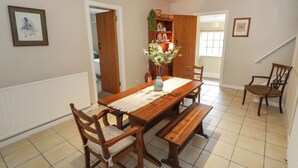 Uma área de refeições com uma mesa de madeira, bancos e cadeiras. Há um vaso com flores sobre a mesa.
