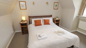 Uma cama bem arrumada com roupa de cama branca e laranja, duas mesas de cabeceira com abajures e quadros nas paredes.