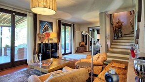 A spacious living room with a large window, a fireplace, and a staircase leading to an upper level. - Villa Barbarella - Villa with private pool (San Gimignano)