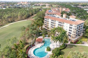 A multi-story hotel with a swimming pool, surrounded by palm trees and a golf course. - Tiburon Ritz Carlton Retreat Condo Rented Monthly With All The Amenities  (Naples)