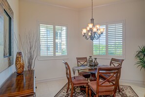 A dining area with a round table, chairs, a chandelier, and a vase on a wooden sideboard. - Tiburon Ritz Carlton Retreat Condo Rented Monthly With All The Amenities  (Naples)