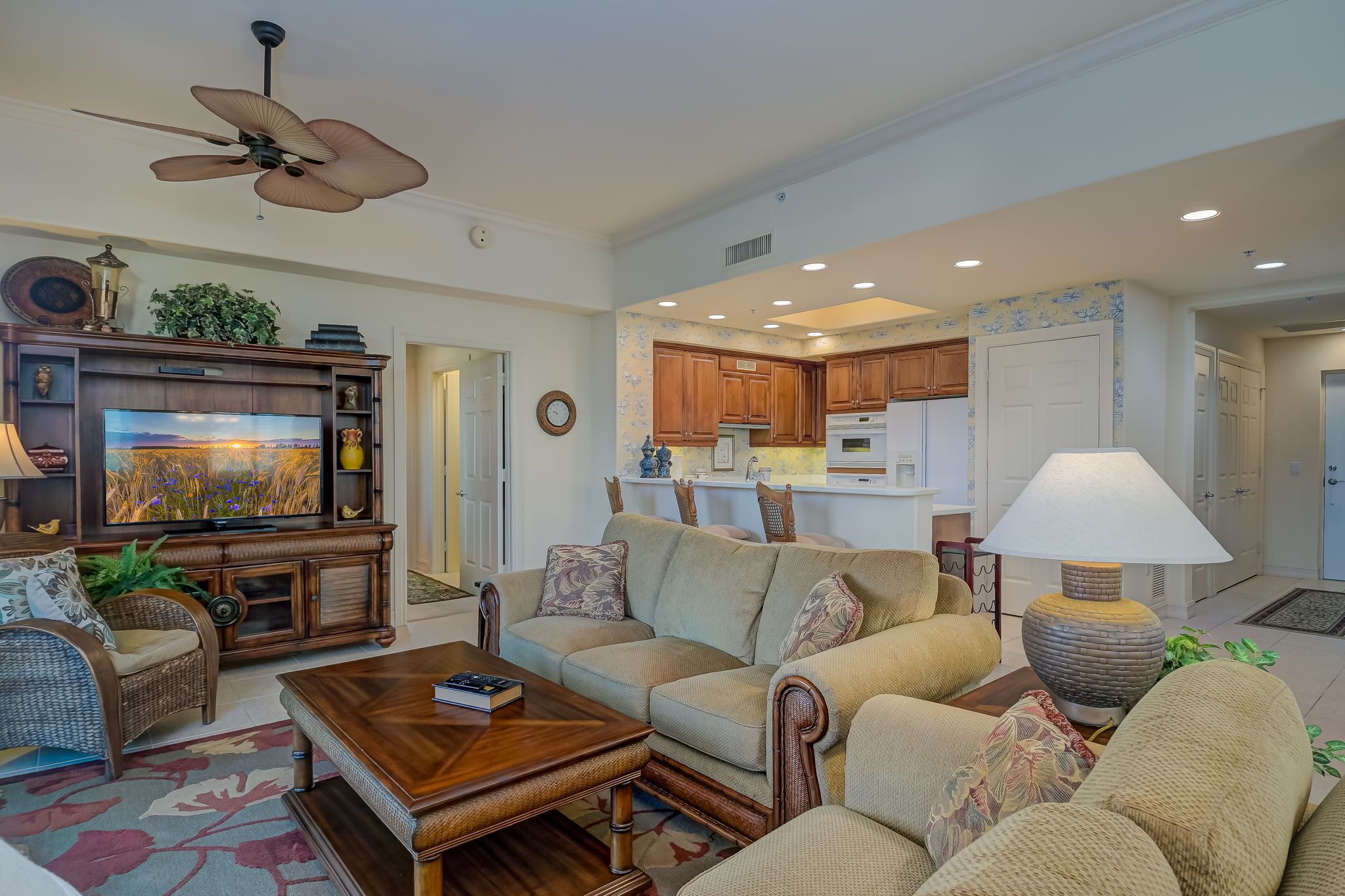 A spacious living room with a large flat-screen TV, comfortable seating, and a ceiling fan.