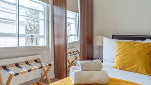Ein Hotelzimmer mit einem Bett, einer gelben Decke, einem Wäscheständer aus Holz und einem Kleiderschrank.