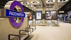 Ein moderner Bahnhof mit einer auffälligen, violetten Beschilderung mit dem Schriftzug "PADDINGTON" und einer Rolltreppe im Hintergrund.