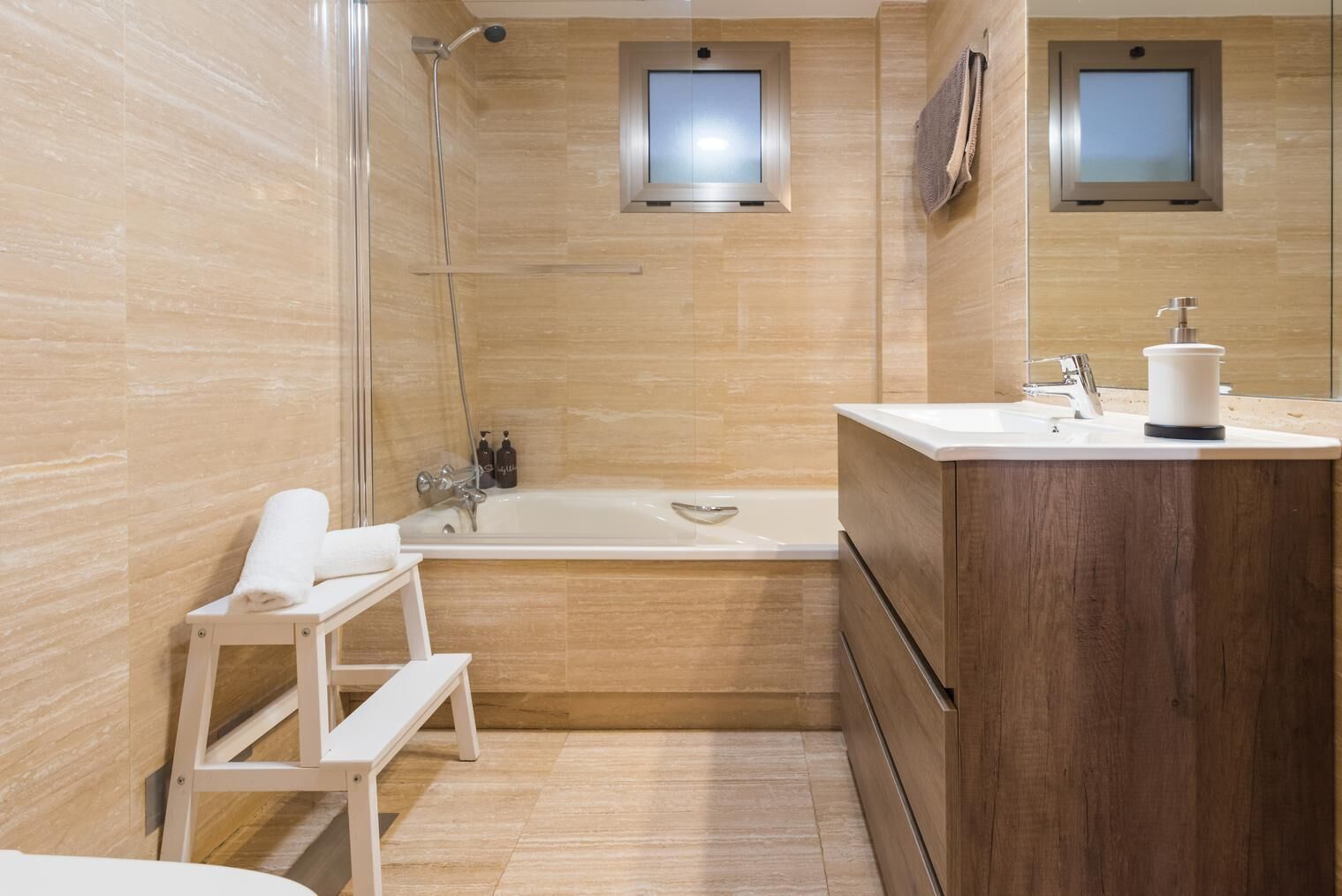 Ein modernes Badezimmer mit Badewanne, Holzwaschtisch, Dusche und einem kleinen Hocker.