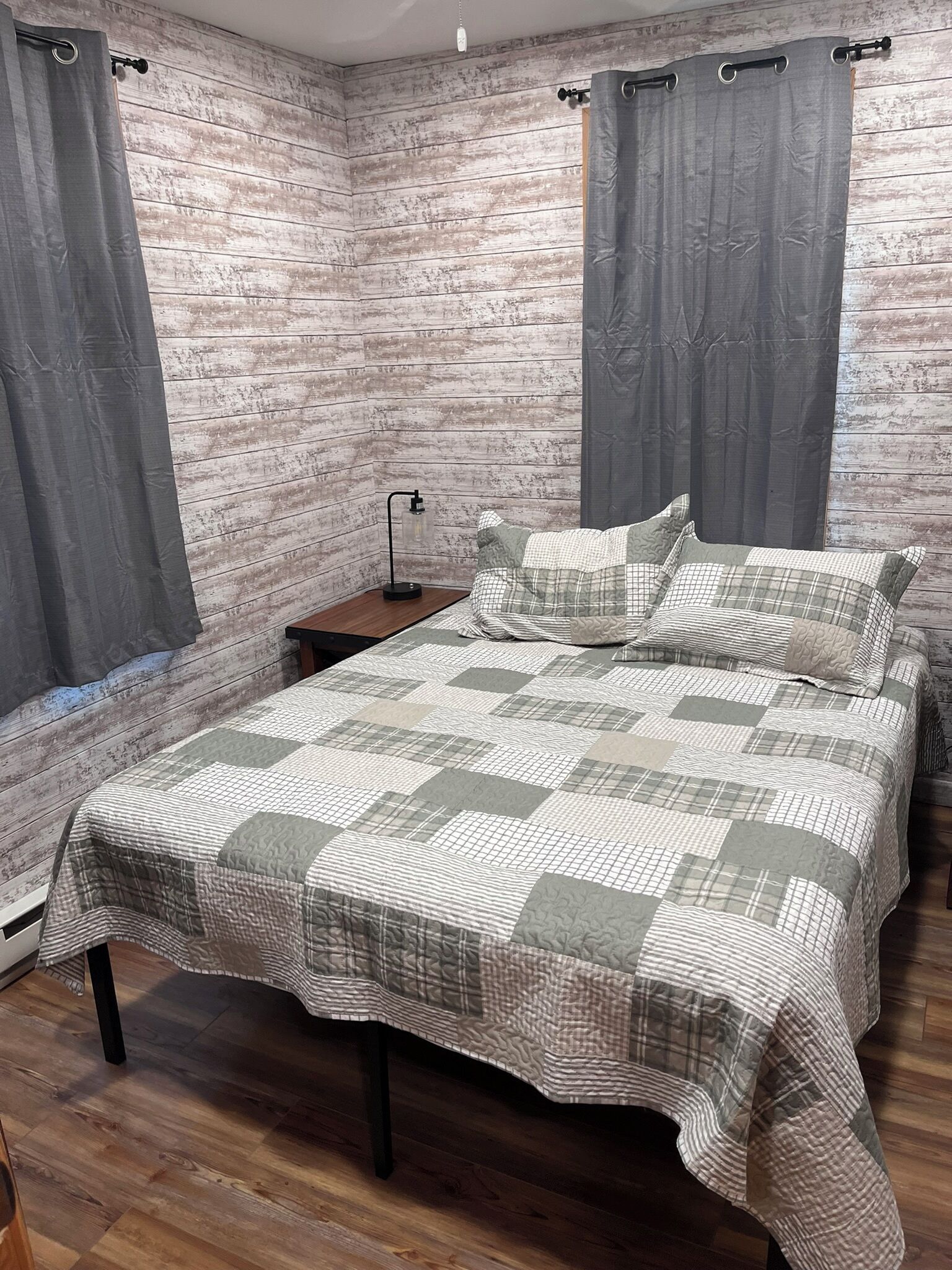 Une chambre avec un plancher en bois, un lit recouvert d’une courtepointe, deux tables de chevet et des rideaux.