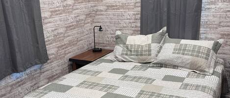 Une chambre avec un plancher en bois, un lit recouvert d’une courtepointe, deux tables de chevet et des rideaux.