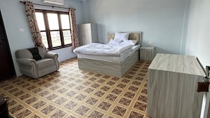 Ein Schlafzimmer mit Bett, Stuhl, Schreibtisch, Deckenventilator und gemustertem Boden.
