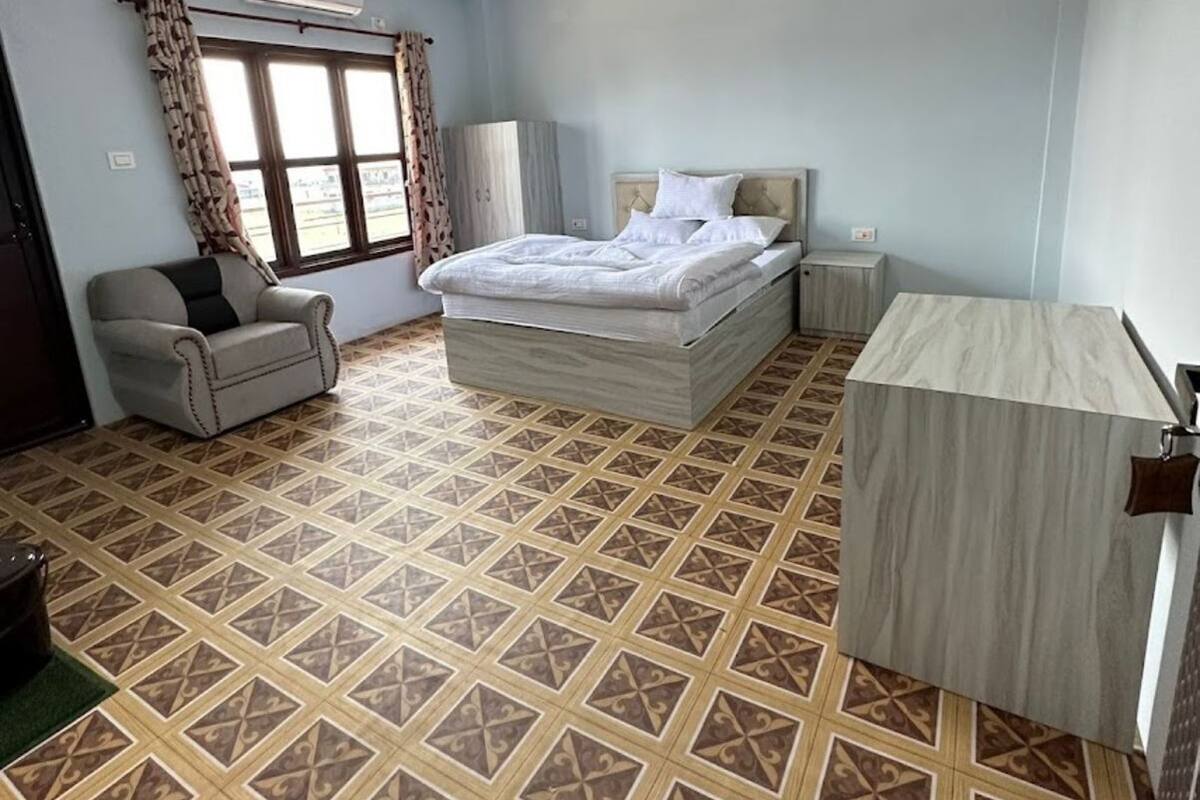 Un dormitorio con una cama, una silla, un escritorio, un ventilador de techo y suelo estampado.