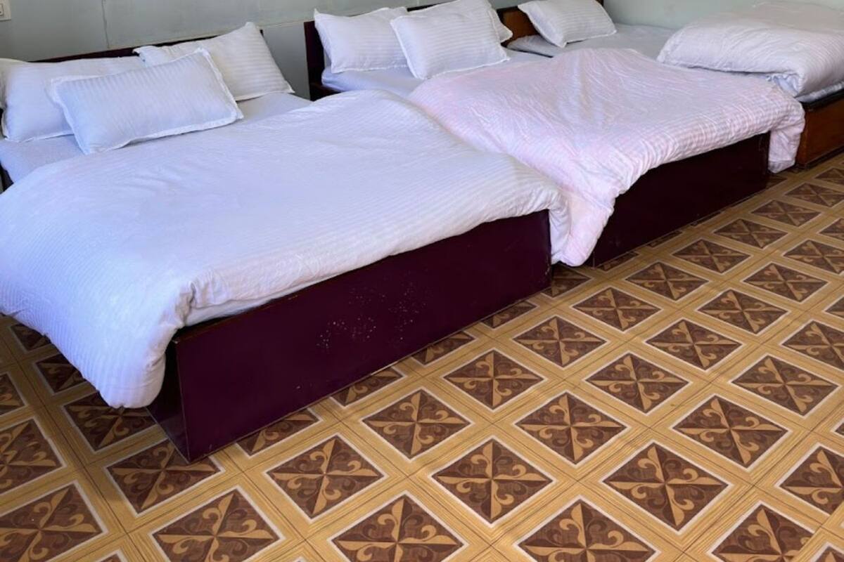 Una habitación con tres camas alineadas, cada una con ropa blanca y cabeceros. Las paredes son de color azul claro y el suelo tiene un diseño de baldosas estampado.