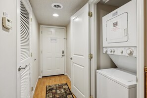 A laundry room with a front-loading washer and dryer, a door with a warning sign, and a vented wall unit. - 2BR Sleeps 6 with Balcony, Recliner & Keurig for Your Morning Brew! (Pigeon Forge)