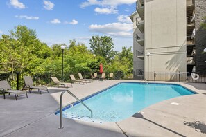 A swimming pool with lounge chairs and a building in the background. - 2BR Sleeps 6 with Balcony, Recliner & Keurig for Your Morning Brew! (Pigeon Forge)