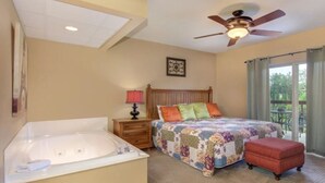 A bedroom with a large bed, a separate bathroom with a bathtub, a ceiling fan, and a view of the outdoors through a sliding glass door. - Top-Floor Riverfront – 3BR Condo with Elevator Access & Double Vanities (Pigeon Forge)