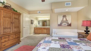 A bedroom with a wooden dresser, a bed with a floral quilt, a vanity with a mirror, and a painting of the Eiffel Tower. - Top-Floor Riverfront – 3BR Condo with Elevator Access & Double Vanities (Pigeon Forge)