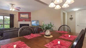 A dining room with a wooden table set for four, red placemats, a potted plant, and a fireplace. - Top-Floor Riverfront – 3BR Condo with Elevator Access & Double Vanities (Pigeon Forge)