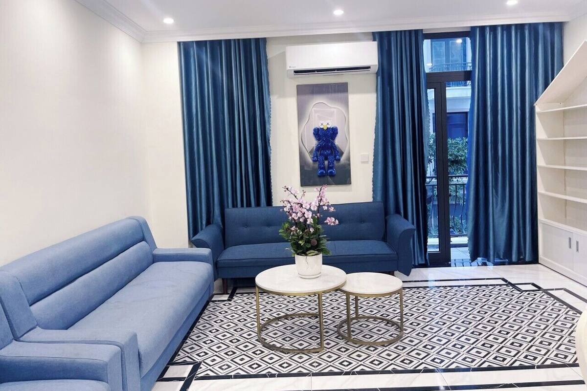 A modern living room with a blue sofa, two small round tables, and a decorative plant.