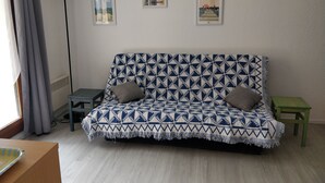 Olohuoneessa on kuviollinen sohva, pieni pöytä, vihreä jakkara ja seinäkello.