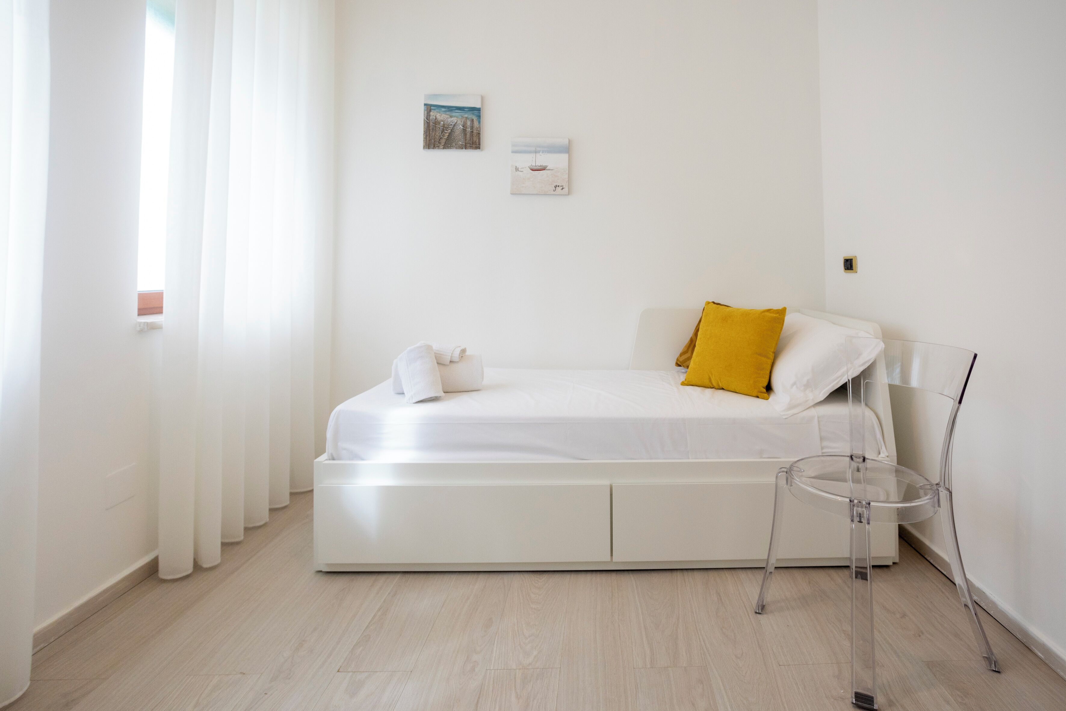 Een minimalistisch ingerichte slaapkamer met een bed, een transparante nachtkastje en twee foto's aan de muur.