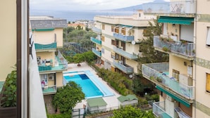 A residential building with a swimming pool, balconies, and a view of the sea.