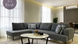 A modern living room with a grey sectional sofa, a round coffee table, and a dining area with a table and chairs. - Kease Qirwan B-11 Royal touch  XZ13 (Riyadh)