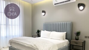 A modern bedroom with a grey upholstered bed, bedside tables with lamps, and a large window with sheer curtains. - Kease Qirwan B-11 Royal touch  XZ13 (Riyadh)