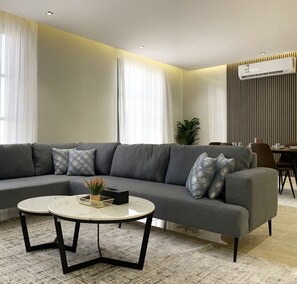Ein modernes Wohnzimmer mit einem grauen Ecksofa, einem runden Couchtisch und einem Essbereich mit Tisch und Stühlen.