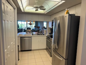 Una cocina moderna con refrigerador de acero inoxidable, horno empotrado y lavavajillas. Se ve un comedor con mesa y sillas a través de una puerta abierta.