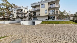 En modern bostadsbyggnad med flera våningar, balkonger, en stenlagd innergård och omgivande grönska.