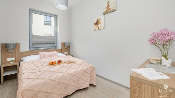 Ett sovrum med en säng, sängbord, ett fönster, konstverk och ett skrivbord med en vas med blommor.