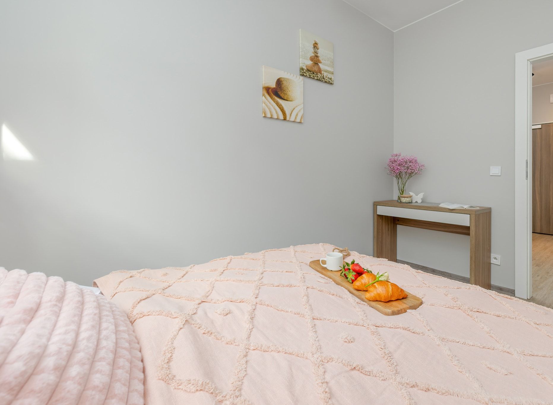 A bedroom with a bed, a bedside table with a vase, and a door leading to another room.