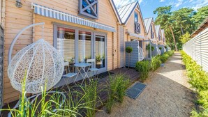 Une rangée de cabanes en bois, chacune dotée d’un petit patio, d’une chaise suspendue et d’un chemin bordé de verdure.