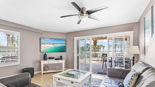 A modern living room with a ceiling fan, a flat-screen TV, a white coffee table, and a grey sofa. - Amalfi Coast 108A- Community Pool, Great Amenities, Steps to Beach! (Miramar Beach)
