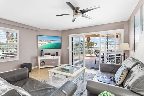 Un salon moderne avec un ventilateur de plafond, un téléviseur à écran plat, une table basse blanche et un canapé gris.