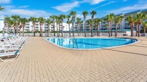 A swimming pool with lounge chairs and palm trees, surrounded by a hotel building. - Amalfi Coast 108A- Community Pool, Great Amenities, Steps to Beach! (Miramar Beach)