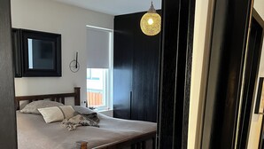 Ein Schlafzimmer mit einem Bett, einer Pendelleuchte, einem Spiegel und einem Fenster.