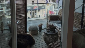 Ein Balkon mit Korbmöbeln, Blumentöpfen und Blick auf ein Hotelgebäude mit Beschilderung.