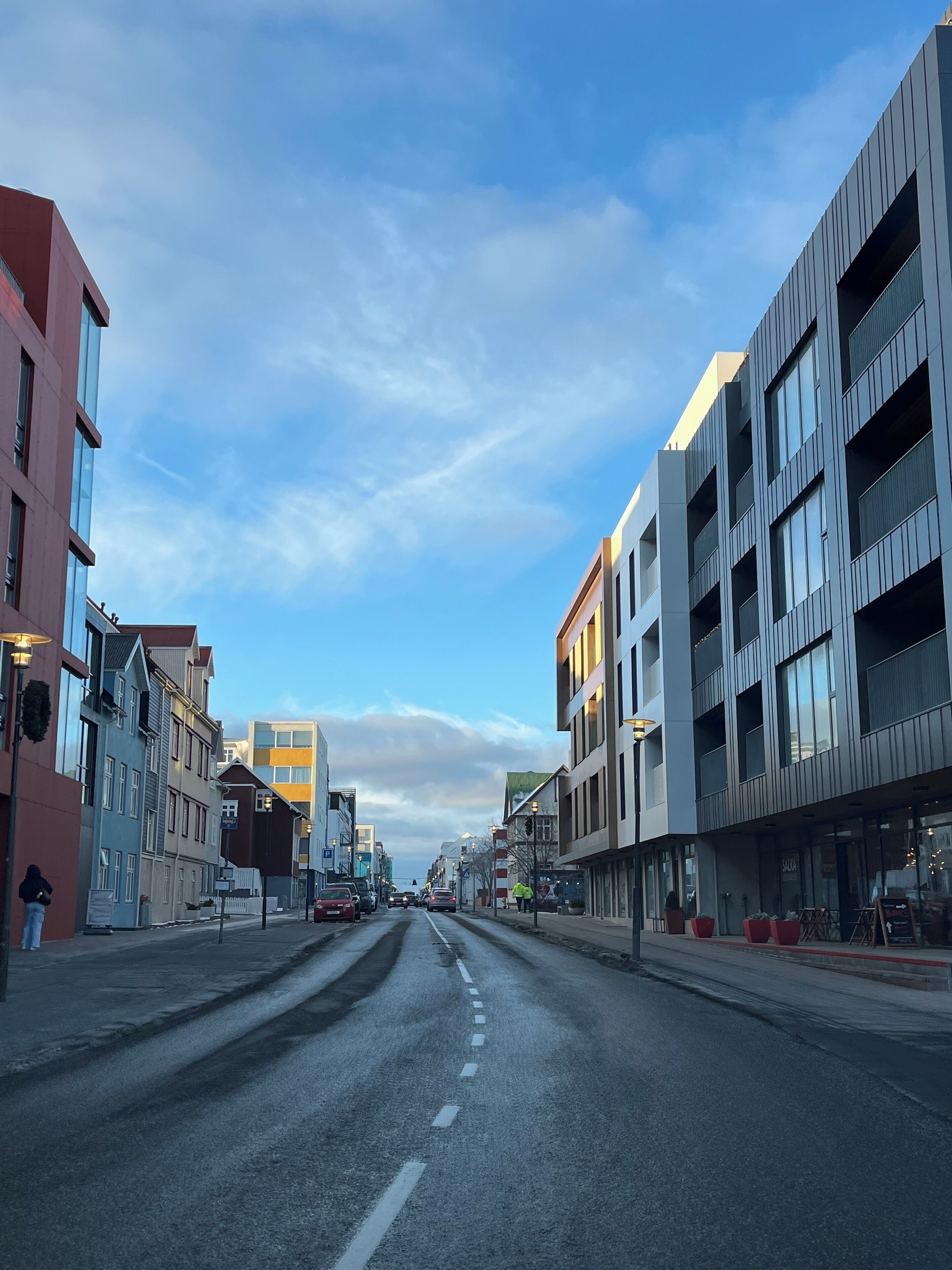 A street with modern buildings, a clear sky, and a road with vehicles.