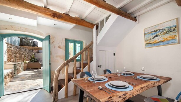 Comedor con mesa de madera dispuesta para cuatro personas, una escalera y vistas al exterior.